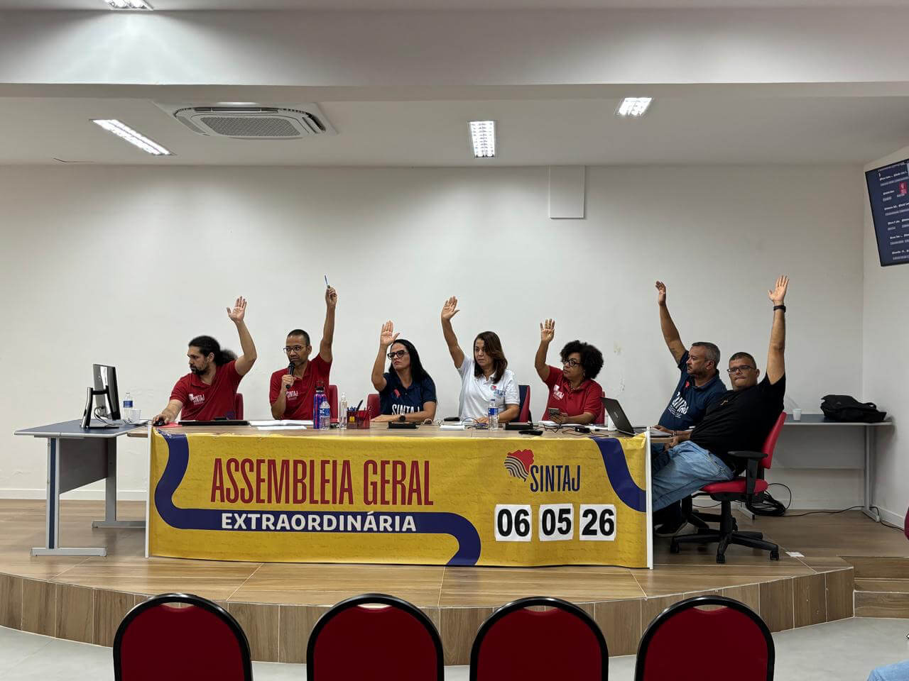 Integrantes da coordenadoria do SINTAJ com as mãos levantadas durante votação em assembleia geral extraordinária